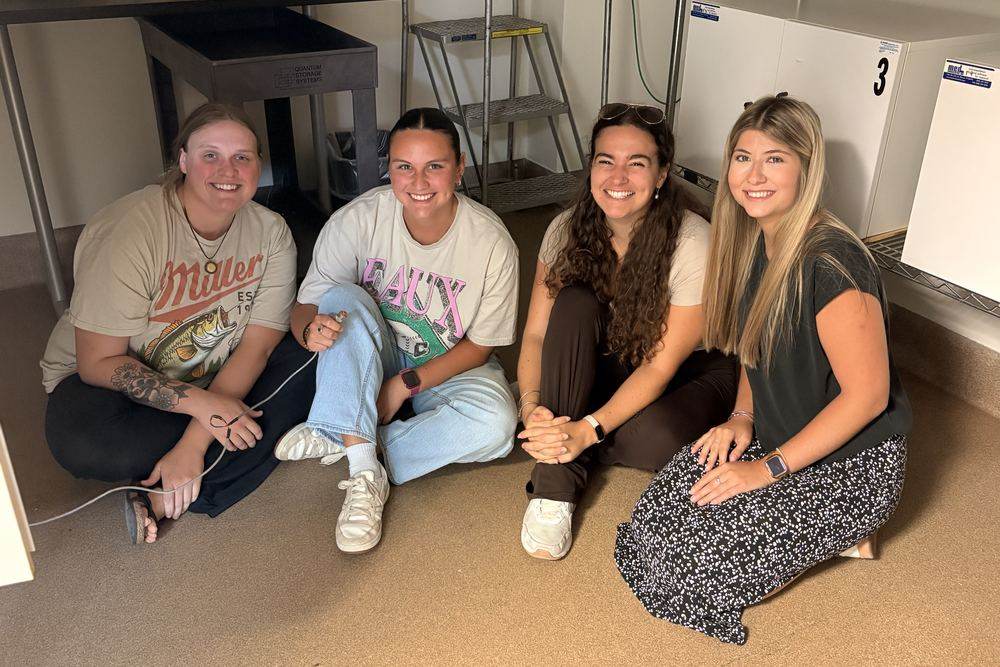 Four lab members sitting on the floor of the lab beside equipment